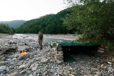 Building of a shelter made of stone near a mountain river, steak fried on fire